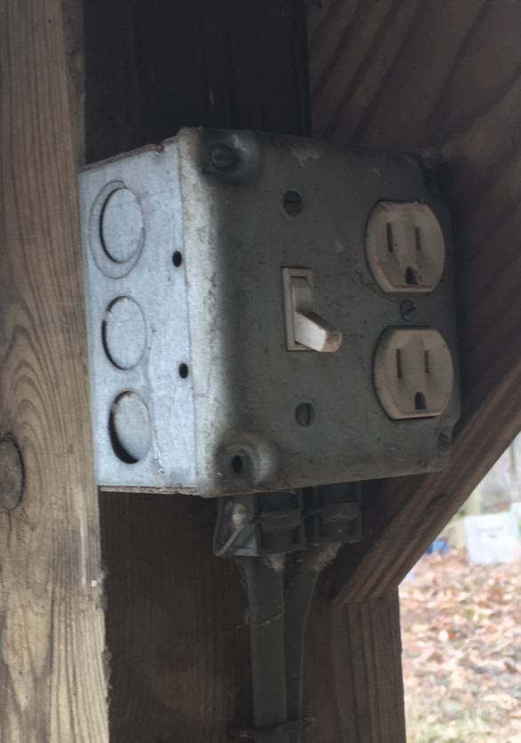 A square metal box containing a regular snap switch and a regular duplex 
	receptacle, with an indoor-style surface-mount cover, mounted to the surface of an outdoor post